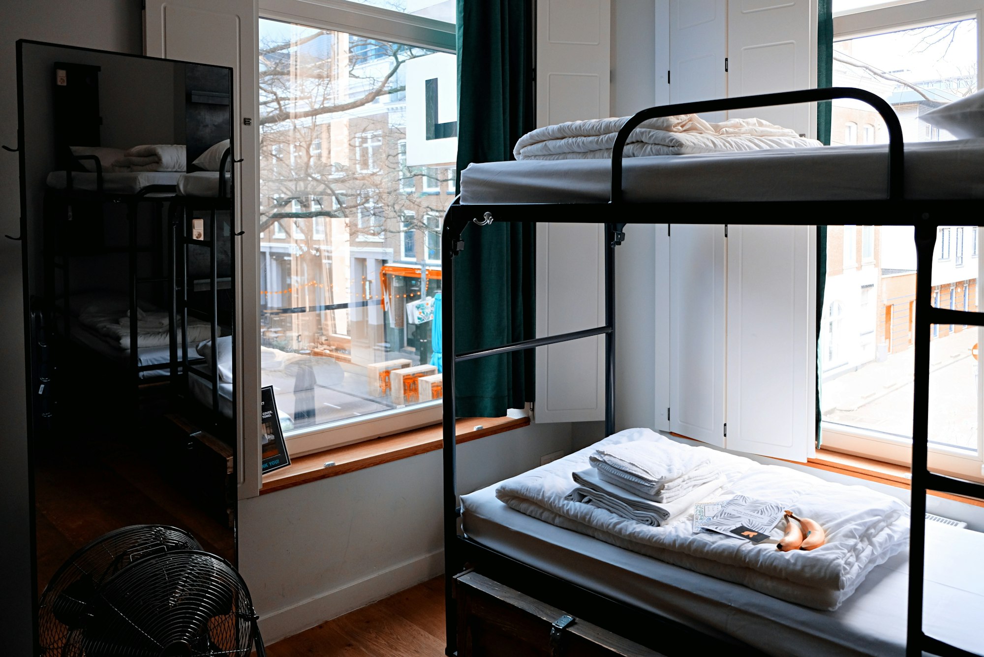 Bunk beds with fresh linen folded on them, in a hostel dorm by the window